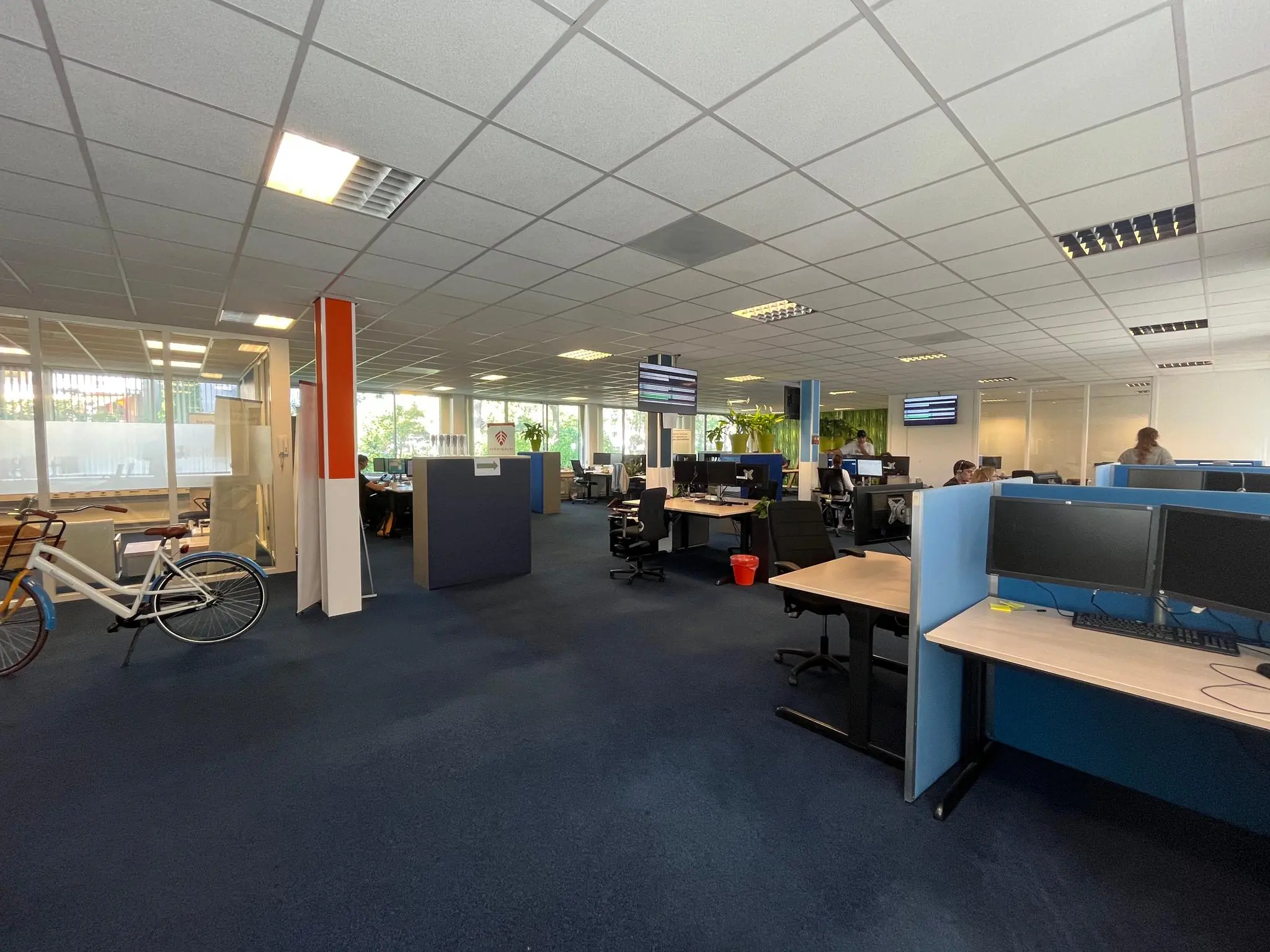 Ruim en modern kantoor met open werkplekken, computers en een fiets bij de ingang aan de Jan van Eycklaan.